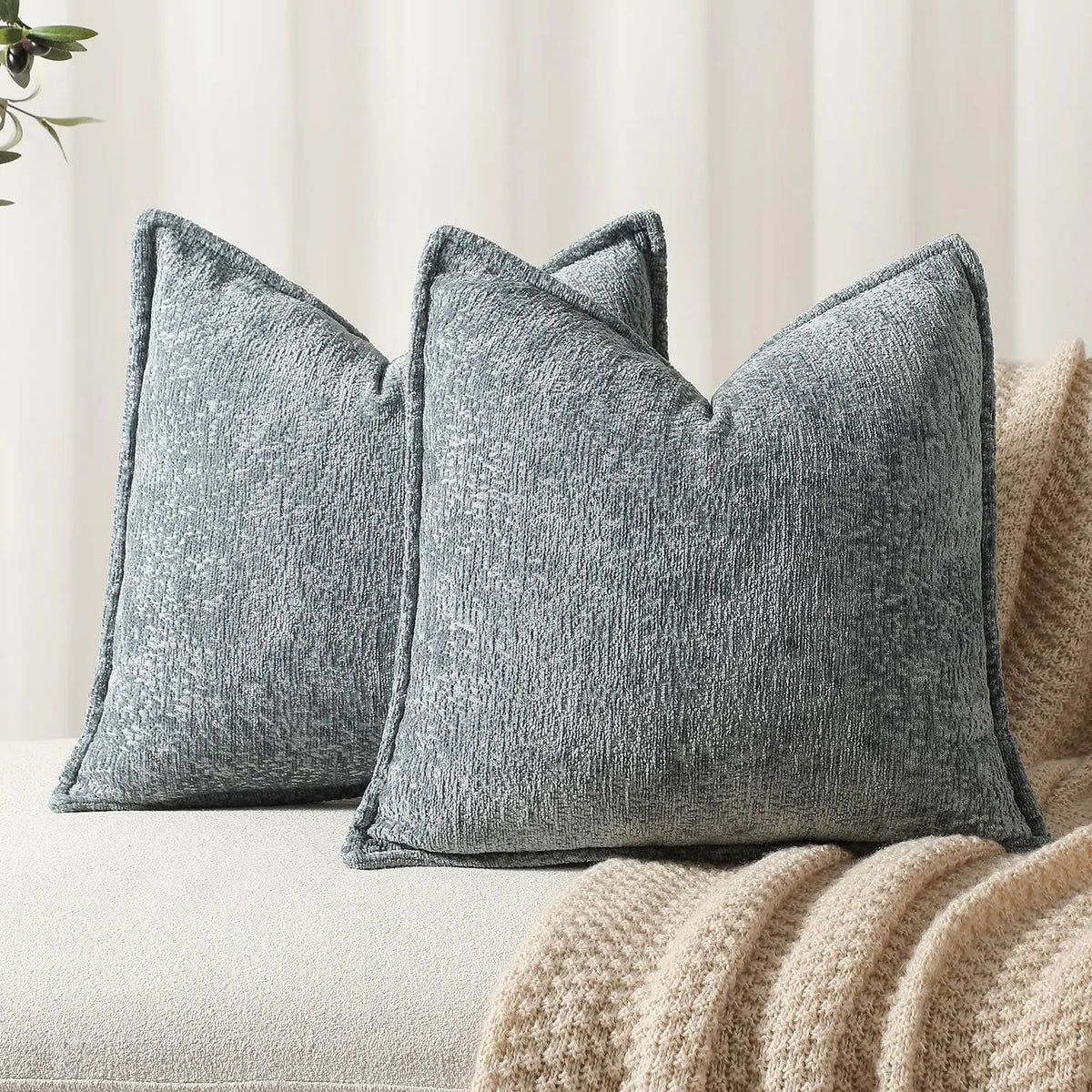 A pair of gray chenille decorative throw pillows resting on a light-colored sofa or bed.
