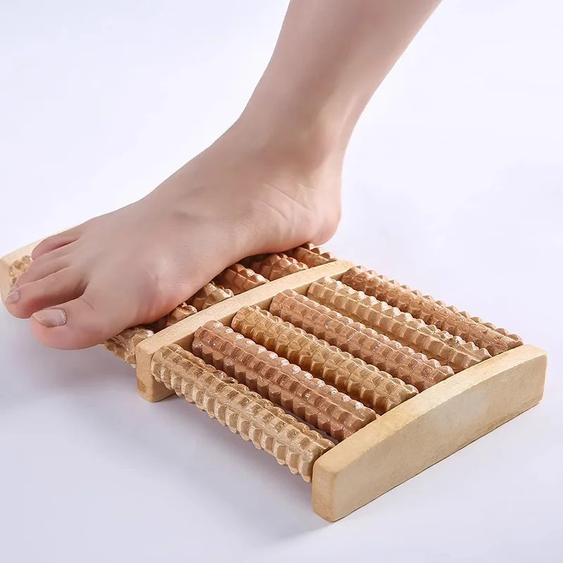 A wooden foot massage roller is shown with a foot resting on it for reflexology and tension relief.