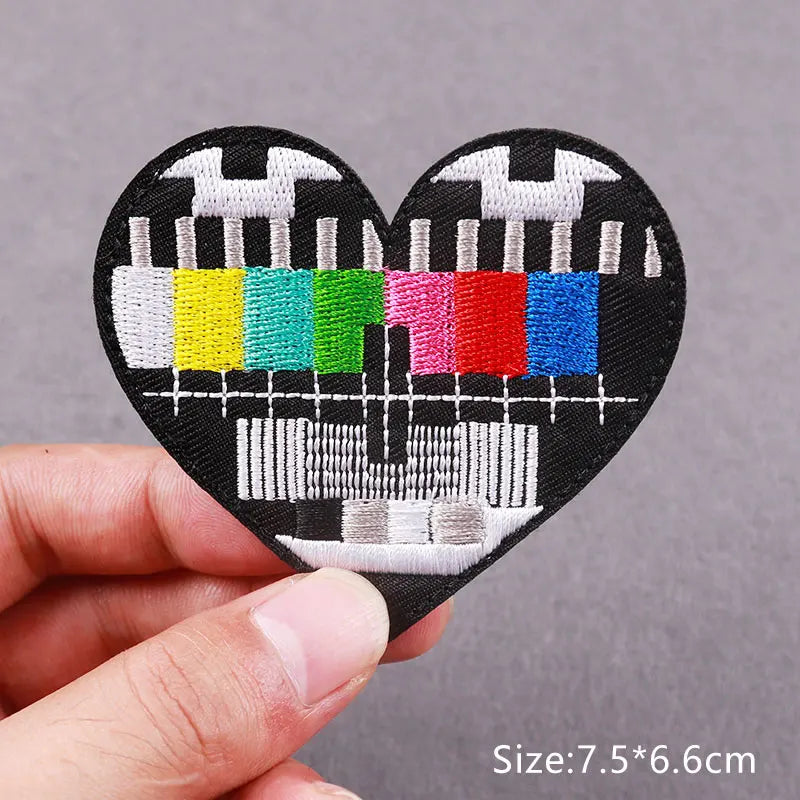 A black heart-shaped patch embroidered with various colored skull and horror motifs on a hand.
