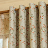 A set of beige blackout curtain panels featuring an orange and green plant pattern hanging on a wooden rod.