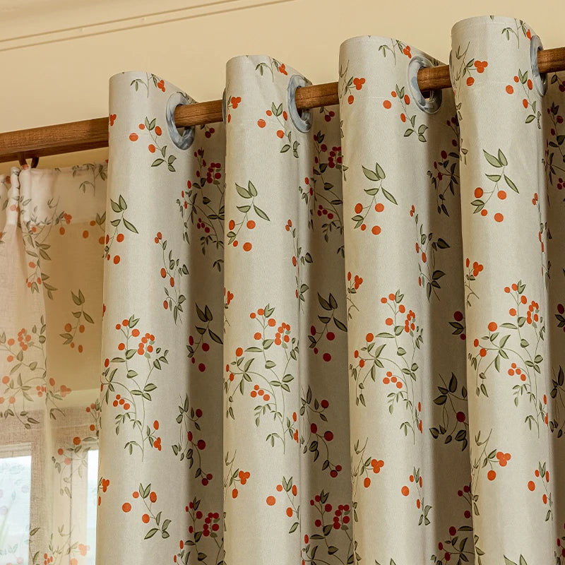 A set of beige blackout curtain panels featuring an orange and green plant pattern hanging on a wooden rod.