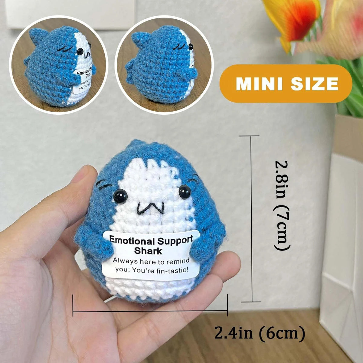 A hand holds a blue and white crocheted shark figurine with an emotional support message.
