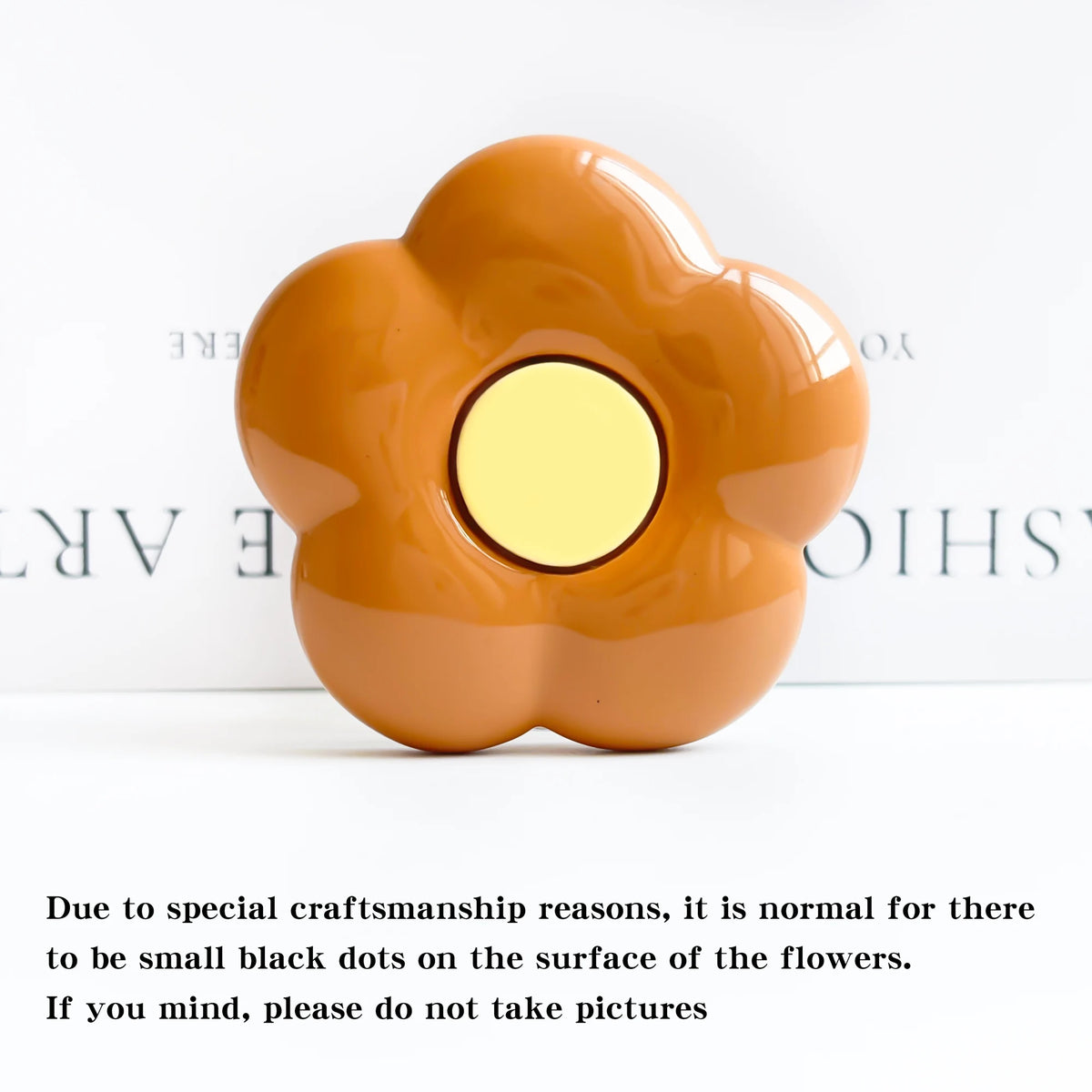 A smooth, orange-colored flower-shaped phone grip stand with small black dots on the surface.