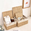 A natural woven rattan storage basket with a lid is shown holding various items like books and small decorative objects.