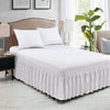 White elastic wrap-around bed skirt with ruffles on a bed in a bedroom setting.