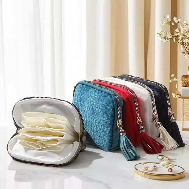 A collection of velvet jewelry organizer bags in various colors like blue, red, and black with tassels displayed on a white m