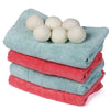 A stack of three white natural wool dryer balls resting on a teal towel.