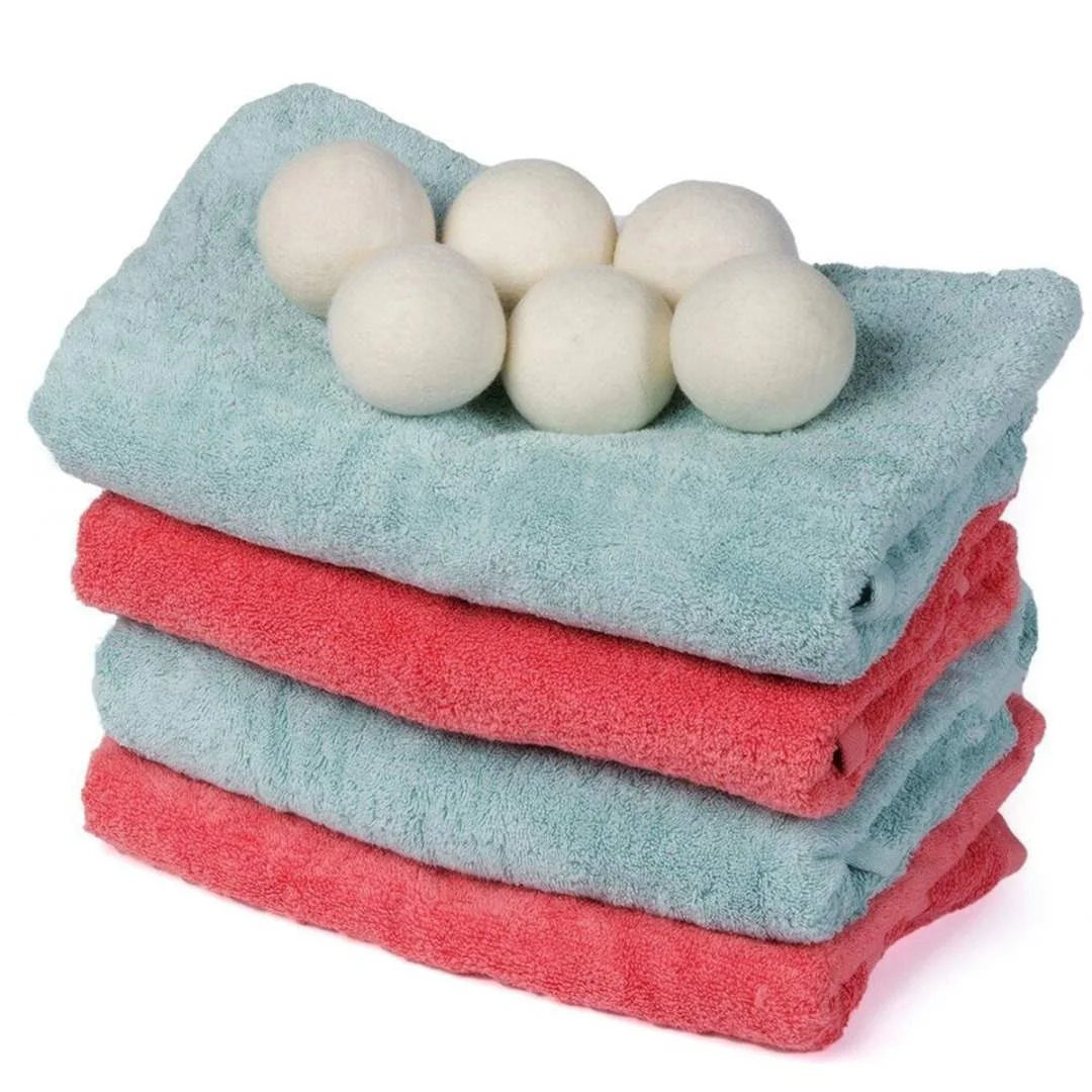 A stack of three white natural wool dryer balls resting on a teal towel.