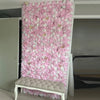 A vertical wall panel covered entirely in pink and white silk rose flowers, displayed next to a bench.