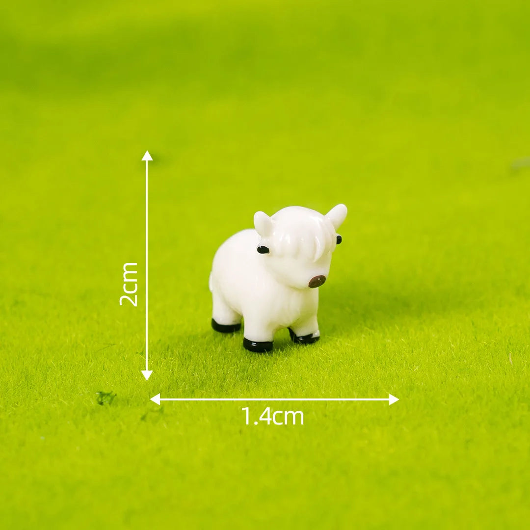 A small white resin Highland cow figurine standing on green grass with a measurement scale.