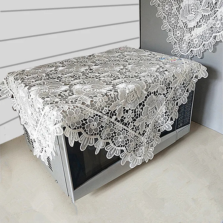 A silver lace tablecloth with an embroidered rose design is displayed on a table.