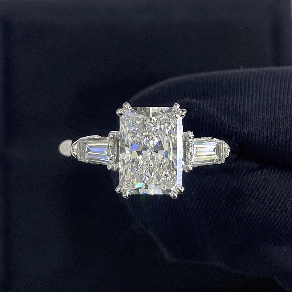 Gros plan d'une bague de fiançailles en moissanite taillée, avec des pierres en baguette, sur fond sombre.