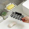 A hand holds a black wall-mounted soap dish with drainage and a white soap bar on a white surface.
