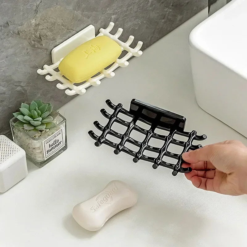 A hand holds a black wall-mounted soap dish with drainage and a white soap bar on a white surface.