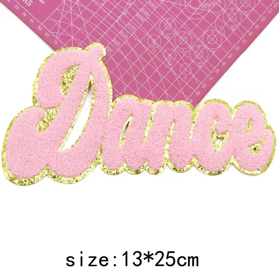 Pink glitter chenille letter patch spelling the word Dance on a pink grid background
