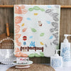 A white cotton face towel embroidered with various cartoon animals and leaves hanging on a wooden rack.