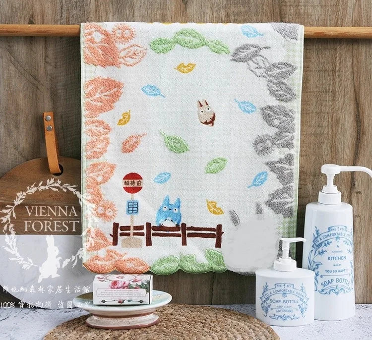 A white cotton face towel embroidered with various cartoon animals and leaves hanging on a wooden rack.