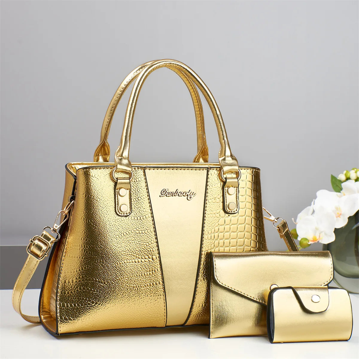 Goldener Krokodilmuster-Patentlederhandtaschenset mit Haupttasche und Clutch.