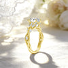 A gold filled moissanite wedding ring featuring a marquise cut diamond and nature-inspired gold setting, resting on a light f