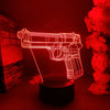 A glowing red gun-shaped night light illuminates a dark surface next to red flowers.