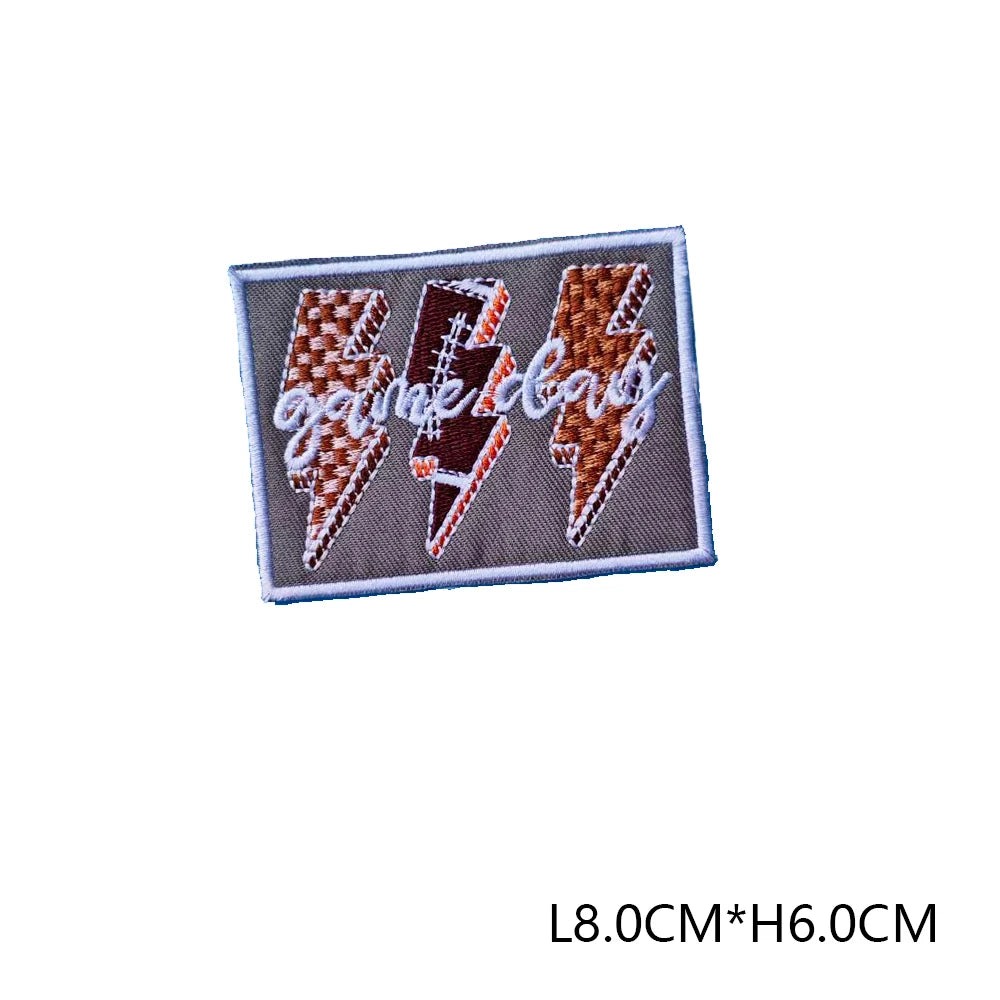 A rectangular embroidered patch featuring the text GAME DAYS in a stylized lightning bolt font on a gray background.