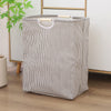 A beige and gray striped foldable laundry basket with wooden handles standing on a wooden floor.