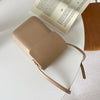 A tan vintage PU leather crossbody shoulder bag resting on a white surface next to an open book.