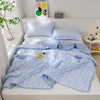 Light blue quilted blanket draped over a bed with pillows and a plant in a bright room.