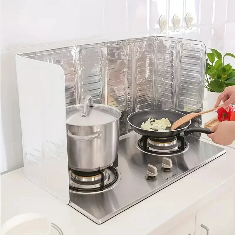 A foldable aluminum stove splatter guard is placed on a stovetop, showing its protective mesh design.