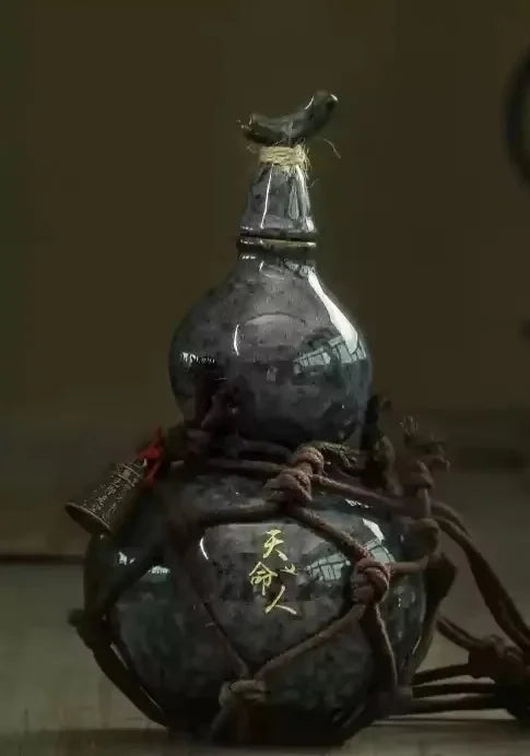A dark ceramic gourd wine set with a stopper and net bag tied with twine.