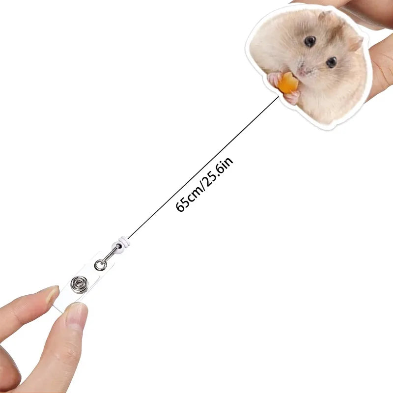 A small, fluffy hamster is shown next to a retractable badge reel with an alligator clip.