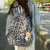 A person is wearing a leopard print nylon backpack with a fluffy bear charm while standing on a sidewalk.