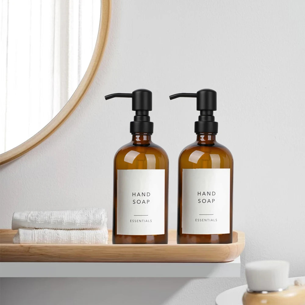 A set of amber glass hand soap dispensers with black stainless steel pumps displayed on a wooden shelf.