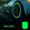 Close-up of a car wheel with a luminous green glow-in-the-dark tire valve cap on a dark road.