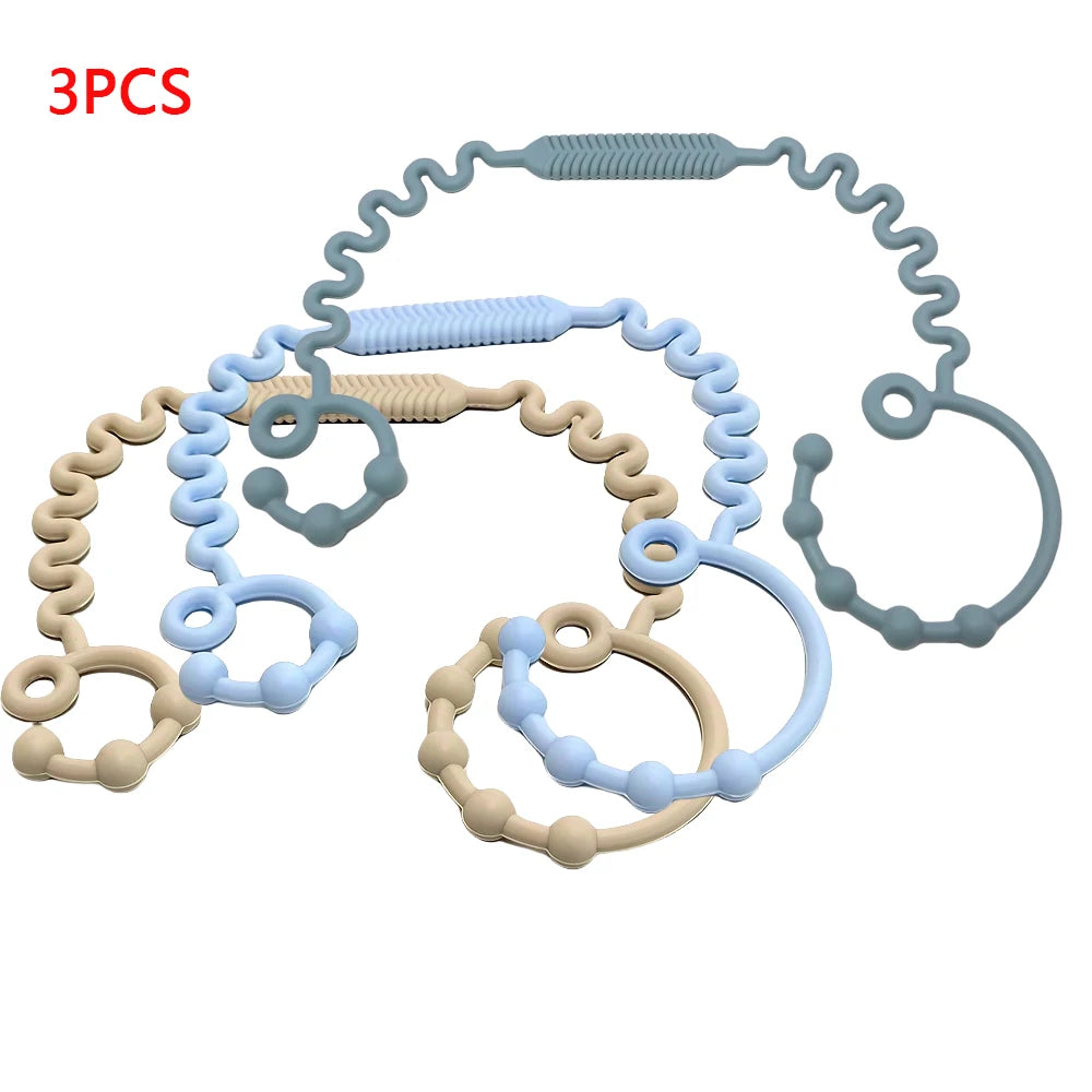 Three silicone pacifier clips or teethers in various shades of blue and beige