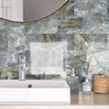 A bathroom wall featuring marble self-adhesive tiles with gray and gold veining behind a white sink.