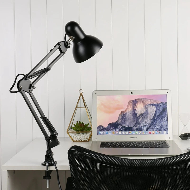 A black adjustable swing arm desk lamp is positioned over a laptop on a white desk.