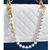 Gold and pearl necklace with a letter C charm displayed against a white quilted purse.