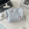 A light blue and white striped makeup bag with red floral embroidery resting on a white desk next to a laptop.