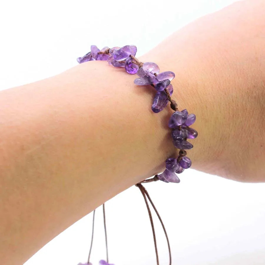 A bracelet made of purple amethyst quartz chips is braided onto a person's wrist.