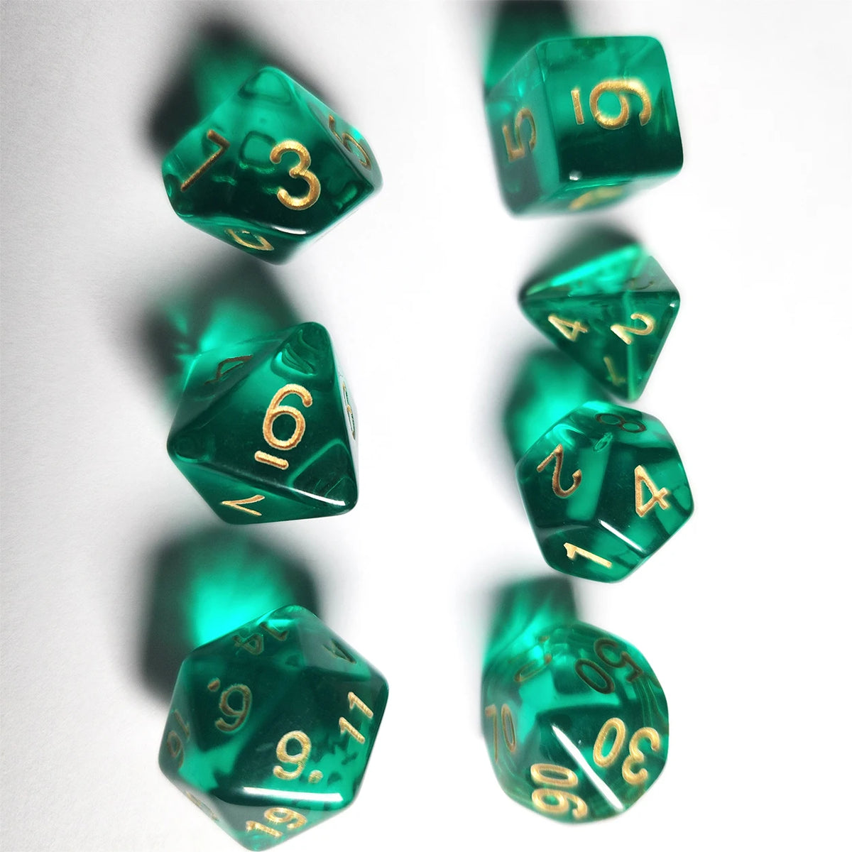 A collection of seven translucent green acrylic polyhedral dice arranged against a white background.