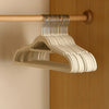A light beige wooden hanger with silver velvet non-slip hangers hanging on a wooden rod.