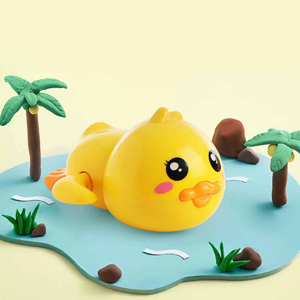 A yellow wind-up bath toy duck with pink accents sits on a blue surface surrounded by small green plants and brown palm leave