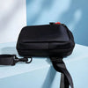 A black compact water-resistant sling bag is shown resting on a light blue surface.