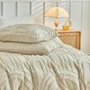 Beige, geprägte Blumen-Decke für Bett mit Lampe und goldener Tasse.
