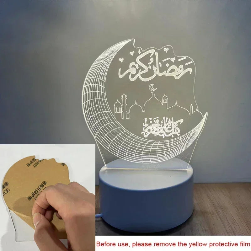 A clear acrylic night light shaped like a crescent moon with Arabic calligraphy and mosque silhouettes resting on a blue base