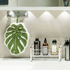 A leaf-shaped coral fleece hand towel with a hanging loop is displayed on a shelf above various bottles.