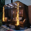 A large, draped canopy featuring warm string lights protecting a garden area with wicker furniture.