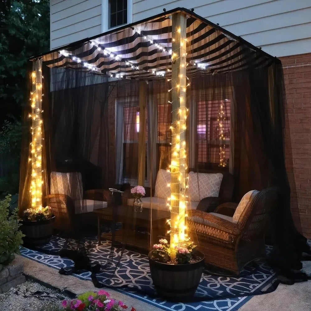 A large, draped canopy featuring warm string lights protecting a garden area with wicker furniture.