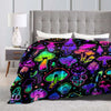 A colorful mushroom print flannel throw blanket displayed on a bed with a white lamp.